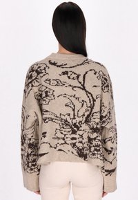Maglione beige con motivo floreale marrone scuro, scollatura rotonda e maniche lunghe. Tessuto morbido con una vestibilità rilassata e lunghezza cropped.
