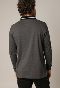 Grijs poloshirt met lange mouwen en een textuurpatroon, voorzien van een zwarte kraag met witte accenten. De achterkant toont een relaxte pasvorm.