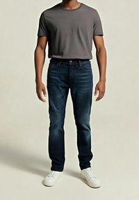 Camiseta gris, vaqueros azules y zapatillas blancas. Los vaqueros presentan un degradado de oscuro a claro, con un diseño clásico de cinco bolsillos y detalles de costuras.