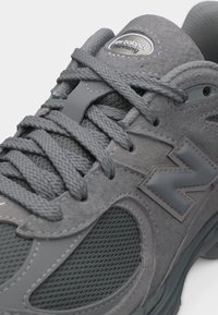 Γκρι παπούτσι τρεξίματος New Balance με υφές από δίχτυ και σουέτ, χοντρές κορδόνια και προεξέχον λογότυπο "N" στο πλάι.