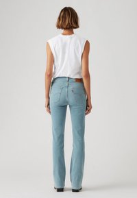 Jeans de mezclilla de un azul claro con pernera acampanada y cintura alta, que cuentan con bolsillos traseros y un parche de cuero marrón con el logo en la cintura.