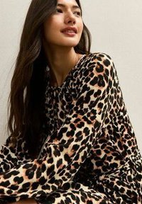 Leopardprint jurk met lange mouwen, gemaakt van een zachte, getextureerde stof in beige en zwarte patronen, met een losse, ontspannen pasvorm.