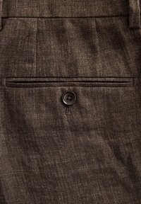 Braun strukturiertes Gewebe mit einem sichtbaren Knopf und einer diskreten Rückentasche. Das Material wirkt gewebt mit einem dezenten Glanz.