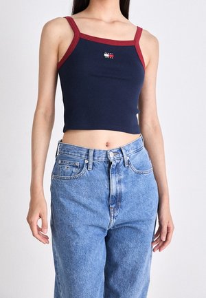 Woman wearing a navy crop top with red trim and Tommy Jeans logo, paired with high-waisted light blue denim jeans.