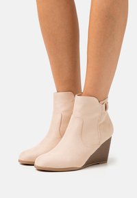 Bottes compensées beige en daim avec une texture lisse, un bout arrondi et une boucle décorative en métal. Talon compensé à texture bois.
