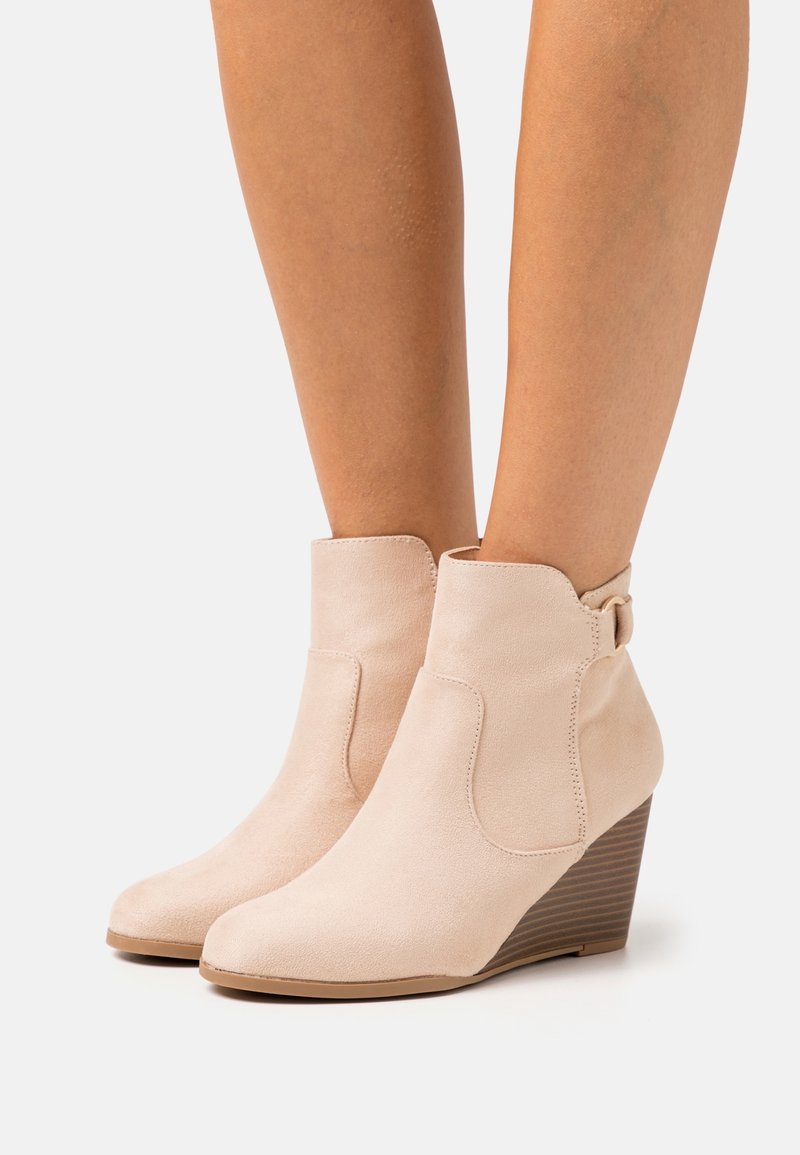 Bottes compensées beige en daim avec une texture lisse, un bout arrondi et une boucle décorative en métal. Talon compensé à texture bois.