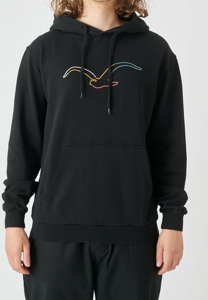 Personne portant un sweat à capuche noir avec une poche kangourou à l'avant et un design minimaliste coloré d'oiseau sur la poitrine, sur un fond uni.
