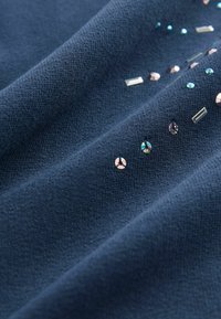 Tessuto blu navy con una superficie testurizzata decorata con vari strass in vetro di forme e dimensioni assortite, che aggiungono interesse visivo.