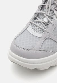 Shoe desportivo cinza claro com uma mistura de couro liso e malha texturizada. Detalhes notáveis incluem uma sola acolchoada e atacadores integrados.
