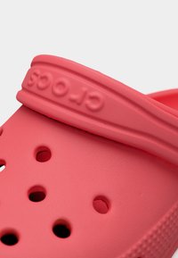 Gros plan sur la bride d'un sabot Crocs rouge avec des trous de ventilation sur la surface supérieure de la chaussure.