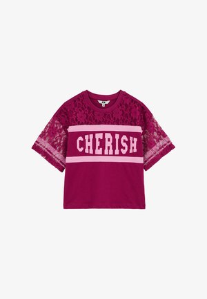 Magenta T-krekls ar mežģīņu piedurknēm, uz kura ir redzams vārds "CHERISH" bold baltajās burtiņās rozā joslas fonā. Mīksta kokvilnas auduma ar smalku ziedu rakstu.