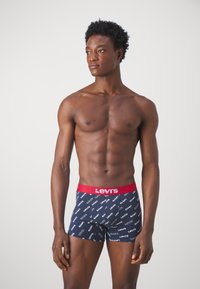 Marinblå boxerkalsonger med röd midja, prydda med upprepat vitt "Levi's" logomönster. Mjukt tyg, åtsittande design och med längd till mitten av låren.