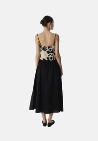 Zwarte maxi-jurk met spaghettibandjes, voorzien van een ingewikkelde crèmekleurige haakwerk-overlay op het lichaam en een geplooide rok. Soepele stofstructuur.