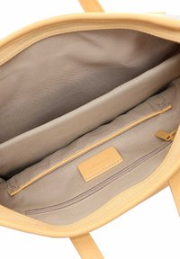 Bolsa de mano amarilla con exterior de cuero suave. Interior de tela beige, que cuenta con un bolsillo con cremallera y una etiqueta de cuero de marca.