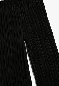 Pantalons plissés noirs avec une taille élastique et une texture lisse, présentant des lignes verticales et un design fluide.