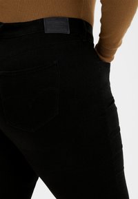 Jeans de mezclilla negra con un diseño ajustado, bolsillos traseros con un patrón de costura distintivo y una etiqueta de marca de cuero en la cinturilla.