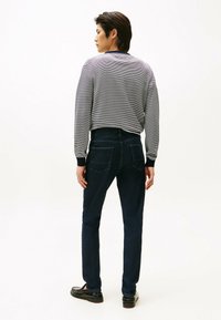 Grijze gestreepte long sleeve shirt en donkerblauwe jeans. Het shirt heeft een geribbelde ronde hals; de jeans hebben een klassieke snit en achterzakken.