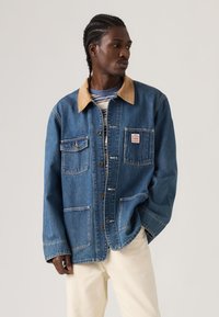 Τζιν μπουφάν με ταμπά, αντίθετο γιακά, εμπρόσθιες τσέπες και κουμπώματα. Φορεμένο πάνω από ριγέ πουλόβερ με άνετη γραμμή.