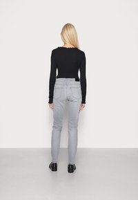 Top negro de manga larga acanalado y jeans ajustados de color gris claro. Presenta un escote en forma de ondas y bolsillos traseros. Combinado con zapatos negros.