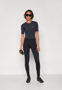 Svart atletisk t-skjorte med korte ermer og tettsittende design, kombinert med svarte høytlivsleggings. Personen holder en manual.