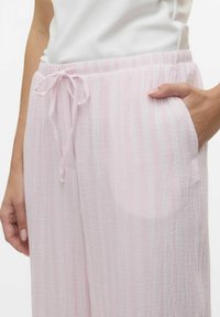 Ljust rosa, lätta tygbyxor med en texturerad yta, med dragsko i midjan och sidofickor. Subtil randig mönster.