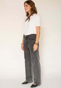 Jean en denim gris taille haute à coupe décontractée, associé à un t-shirt blanc et un bandana marron. Ballerines noires pointues avec des accents argentés.