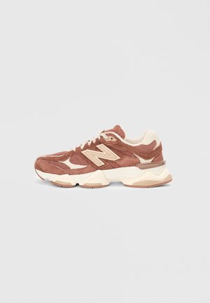 Brown suede sneakers with cream accents, featuring a textured design, lace closure, and a cushioned sole. Classic New Balance logo visible.