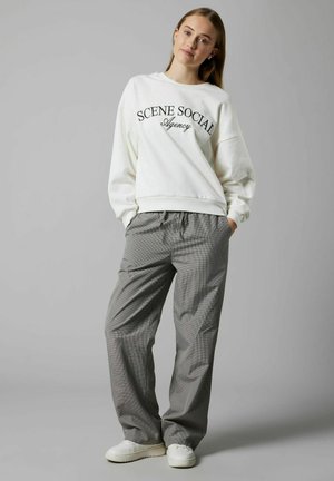 Vit sweatshirt med texten "SCENE SOCIAL Agency", kombinerad med grå rutiga byxor i lös passform och vita sneakers.