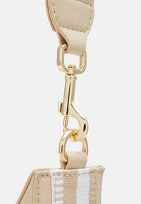 Beżowy skórzany pasek z metalowym klipsem i elementami w odcieniu złota. Posiada teksturowaną powierzchnię oraz szczegółową dekorację w paski.