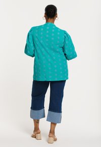Teal geborduurd top met puffmouwen, gecombineerd met donkere denim cropped broeken met contrasterende manchetten. Ontwerp met open rug.