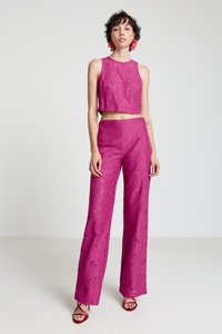 Ensemble deux pièces fuchsia composé d'un haut court et d'un pantalon à jambes larges, fabriqué en tissu texturé avec des motifs ajourés et mis en valeur par des talons à brides.