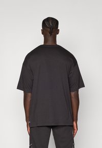 Juodas didelis T-shirt'as, trumpomis rankovėmis, apvaliu iškirpimu, lygaus paviršiaus, be matomų raštų, dėvimas su suderintomis tamsiomis šortais.