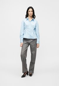 Chemise bleu clair boutonnée avec col, associée à un pantalon gris à jambes larges et des escarpins en cuir verni noir.