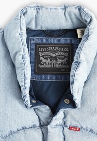 Giacca di jeans azzurro chiaro con colletto, tessuto bicolore, bottoni a pressione in ottone e etichetta interna del marchio Levi's nera. Taglia M.