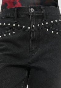 Μαύρα τζιν παντελόνια από τζιν με ασημένιες πέρλες κατά μήκος της ζώνης, με στενή γραμμή και κανονικές μπροστινές τσέπες.