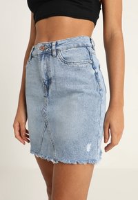 Džínová sukně v světlé modré barvě se zesvětleným vzhledem. Má vysoký pas, zapínání na knoflíky vpředu a třepící se lem. Obsahuje boční kapsy.