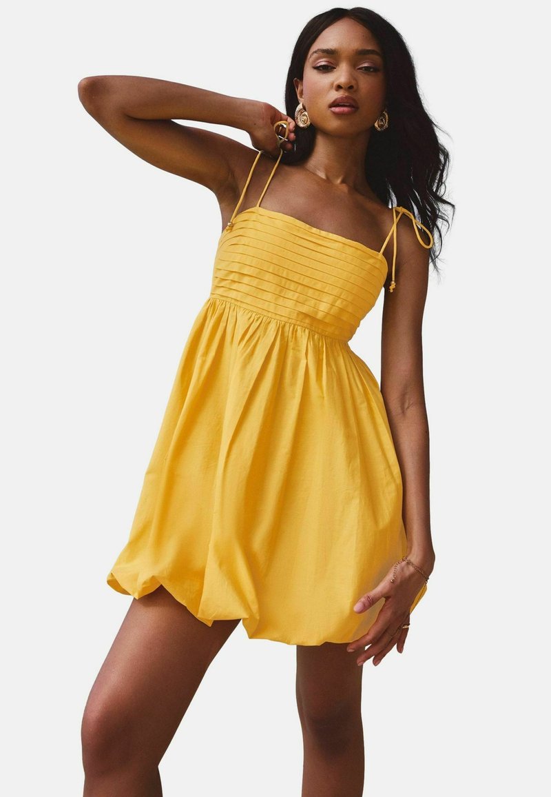 Geel zomerjurk met een aansluitende lijfje, geplooide textuur, gathered taille en verstelbare bandjes. Gladde stof met een uitlopende rok.
