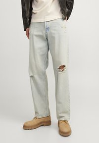 Lyseblå denimjeans med slitte detaljer, inkludert rifter på kne og lår. Kombinert med brune semskede sko og en svart skinnjakke.