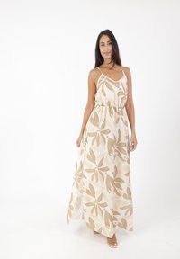 Robe maxi en tissu léger avec des motifs de feuilles beiges et vert olive, taille élastique, fines bretelles et silhouette fluide.