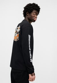 Μαύρο μακρυμάνικο t-shirt από βαμβάκι, με γραφικό σχέδιο στην πλάτη και λευκό κείμενο κατά μήκος των μανσετών.