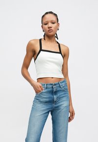 Top alb scurt cu bretele negre, cu decolteu pătrat; asortat cu blugi largi, cu talie înaltă, de culoare albastru deschis. Textură netedă, design minimalist.