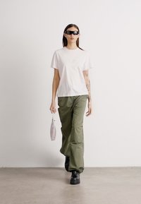 Λευκό βαμβακερό t-shirt με μικρή γραφική απεικόνιση, ελαιοπράσινα φαρδιά παντελόνια, μαύρες πλατφόρμες και ανοιχτό μωβ τσάντα.