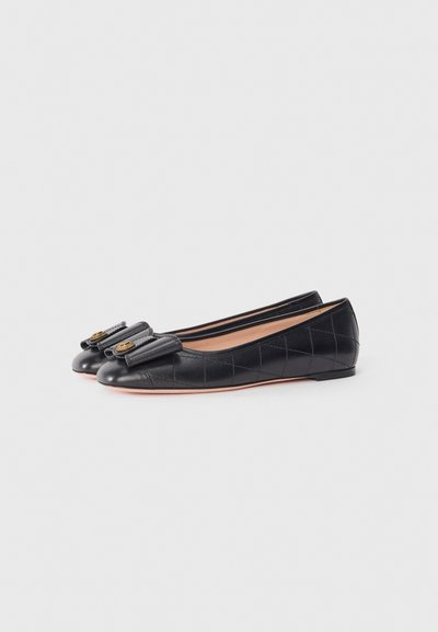 Ballerines en cuir noir avec une texture matelassée, bout rond et un accent en nœud sur l'avant. Semelle plate, conçues pour un usage décontracté.