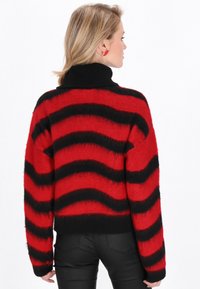 Pulover cu dungi roșii și negre, cu guler înalt cu nervuri, textură moale și croială lejeră. Prezintă modele ondulate pe întreaga țesătură.