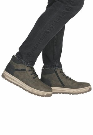 Person trägt dunkle Jeans und graue Schnürstiefeletten mit beigen Sohlen, sichtbare Reißverschlussdetail an einer Seite der Stiefel.