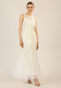 Abito lungo bianco con paillettes, sovrapposizione trasparente all'ascella e silhouette a sirena. Tulle morbido all'orlo, minimalismo nei dettagli.
