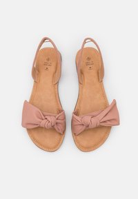 Sandali rosa pallido con dettaglio a fiocco annodato, aperti sul retro e con suole in tonalità miele. Realizzati in materiale morbido con suola piatta e accenti cuciti.