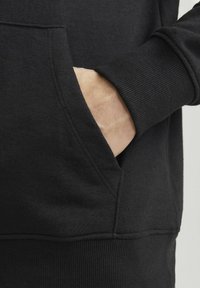 Black hoodie featuring a kangaroo pocket, ribbed cuffs, and hem, made from a soft fabric with a smooth texture. Minimalistic design.