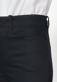 Svarta byxor med en stilren design, som har slät front, sidofickor, platt midja och ett mjukt, strukturerat tyg.