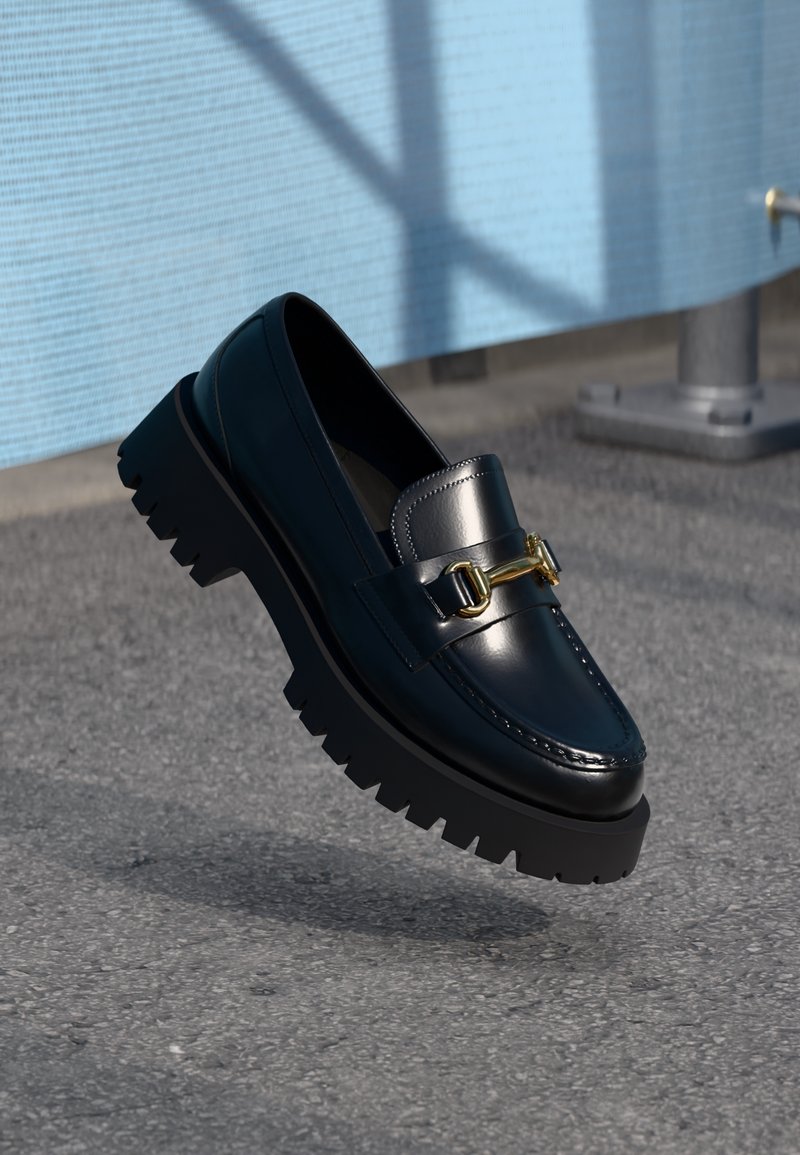 Bottines en cuir noir au fini brillant, avec un détail de boucle en or proéminent et une semelle en caoutchouc épaisse et texturée.